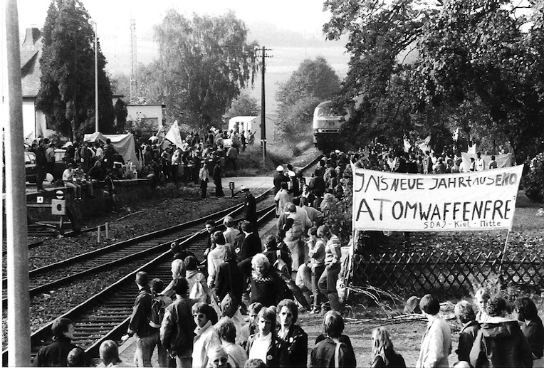 Demonstrierende an einer Bahnstrecke mit einem Transparent „atomwaffenfrei“